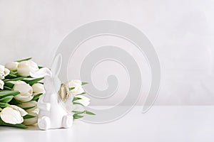 Easter rabbit figurine with bouquet of white tulips on white background. Easter celebration concept. Copy space. Front view