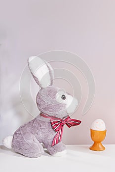 Easter rabbit toy and a cheerful egg in a nest on a white gray background