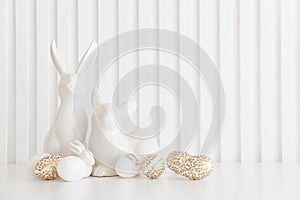 Easter rabbits figurines and eggs on white background. Easter celebration concept. Copy space. Front view