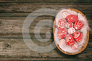 Easter red eggs with folk white pattern lay on feather into basket in the right side of rustic wood table. Top view. Ukrainian tra