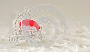 Easter red painted egg in a small souvenir baby stroller on a white background with white fluffy feathers.