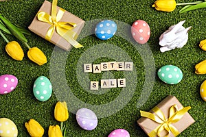 Easter sale banner with colorful eggs, gifts, tulips, bunny and sale text on a green grass background