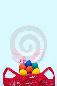 Easter shopping concept. Hand painted Easter eggs, pink bunny ears and a red shopping bag