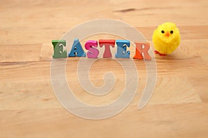 Easter spelt in colourful wooden letters against a natural wooden beige background with a fluffy yellow chick.