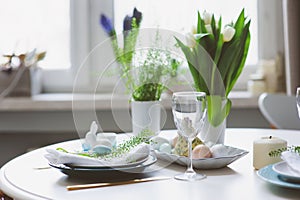 Easter and spring festive table decorated in blue and white tones in natural rustic style, with eggs, bunny, fresh flowers