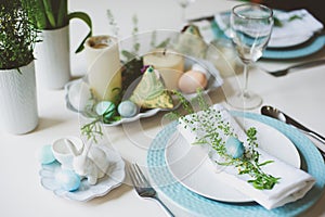 Easter and spring festive table decorated in blue and white tones in natural rustic style, with eggs, bunny, fresh flowers