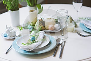 Easter and spring festive table decorated in blue and white tones in natural rustic style, with eggs, bunny, fresh flowers