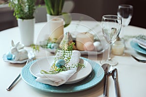 Easter and spring festive table decorated in blue and white tones in natural rustic style, with eggs, bunny, fresh flowers