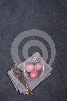 Easter and spring holiday concept. Easter multicolored pastel pink eggs in a glass bowl on a dark background. Flat lay.