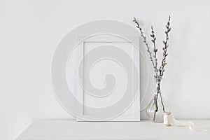 Easter spring still life. Blank vertical picture frame mockup on white wooden table. Blooming pussy willow branches with