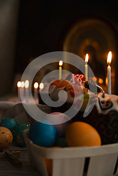 Easter still life with Easter cake and eggs in the basket, burning candles in the darkness of monastry church with