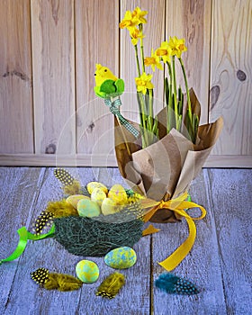 Easter still life with a nest with Easter eggs, yellow daffodil flowers, feathers, decorative chickens, ribbons