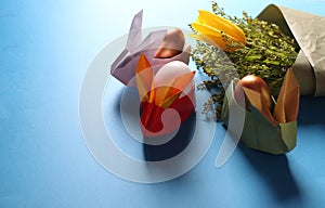 Easter still life. Paper rabbits. Easter Golden eggs. On the blue table, a bouquet of tulips