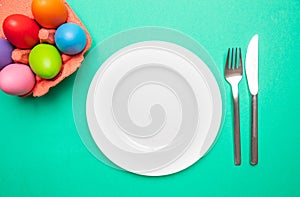 Easter table, place setting. Easter eggs, empty white plate, green background