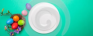 Easter table, place setting. Easter eggs, empty white plate, green background