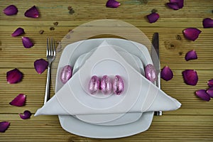 Easter table place setting in white with pink shiny wrapped eggs and purple rose petals and love heart decorations