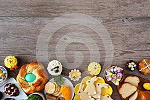 Easter table scene with an assortment of breads, desserts and treats, top view bottom border over a wood background