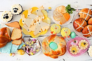 Easter table scene with an assortment of breads, desserts and treats, top view over a white wood background