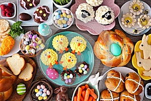 Easter table scene with an assortment of breads, desserts and treats, top view over wood