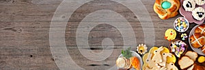 Easter table scene with a selection  of breads, desserts and treats, top view banner with corner border over a wood background