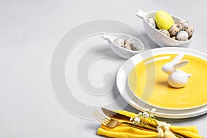 Easter table serving. White yellow dishware, quail eggs, golden cutlery, white ceramic bunny on gray
