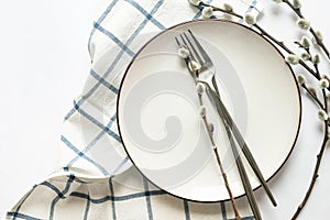 Easter table setting with empty white ceramic plate with cutlery and spring willow branches on white table. Neutral colors