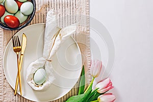 Easter table setting, with napkin folded in shape of a rabbit, blue egg and tulips, top view