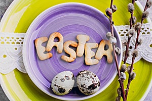Easter table setting. Yellow and pirple plate, cutlery, cookies letter easter