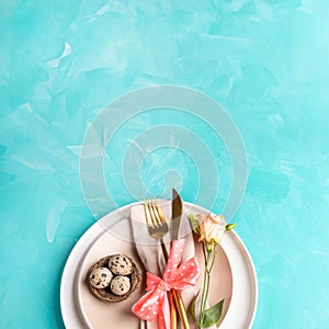 Easter. Top view. Beige plates, nest, quail eggs, golden cutlery, flower on turquoise. Copy space.