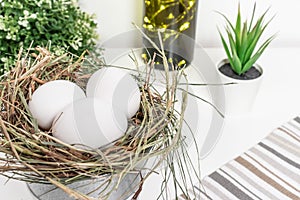 Easter white chicken eggs in straw nest, green spring plants and easter holiday decoration on white background and country style