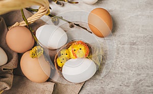 Easter white egg with little chick toys in nest on a grey table, in rustic style