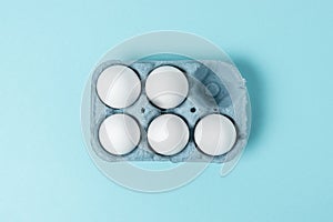 Easter white eggs in carton tray on blue background. Flat lay. Minimal concept