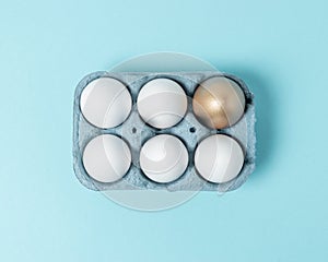 Easter white eggs with gold egg in carton tray on blue background. Flat lay. Minimal concept