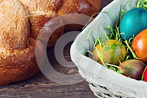 Easter wicker basket with colored eggs and Easter bread on grey wooden board.