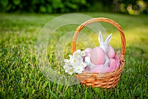 Easter wicker basket with pink eggs, white porcelain bunny and delicate flowers. Happy Easter.