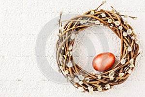 Easter willow wreath with red Easter egg on white tablecloth. Top view