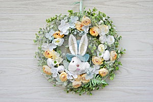 Easter wreath with bunny and flowers hanging on wooden door, close up