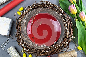Easter wreath, yellow Easter eggs around tulips, gifts and wrapping paper. Inside the wreath stands a beautiful glossy red plate