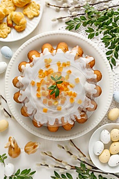 Easter yeast cake babka covered with icing with candied orange peel on a white plate top view.