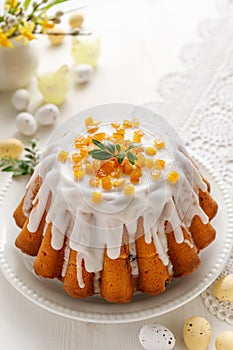 Easter yeast cake covered with icing with candied orange peel on a white plate close up view.