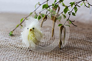 Easter, yellow chick chick stands under blooming birch twigs with green petals