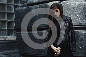 Eastern beautiful woman wearing biker jacket poses in backyard of vintage apartment house