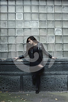 Eastern beautiful woman wearing biker jacket poses in backyard of vintage apartment house