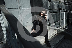 Eastern beautiful woman wearing biker jacket poses in backyard of vintage apartment house