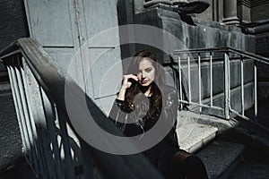 Eastern beautiful woman wearing biker jacket poses in backyard of vintage apartment house