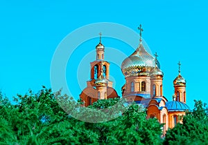 Eastern Church with gold domes or cupolas and orthodox crosses againts blue sky and green trees in Pokrov city park, Ukraine at su