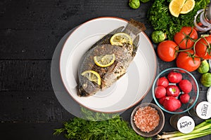 Eastern or European cuisine, Fried fish with fresh vegetables, on a wooden black background. I also eat healthy food. Seafood,