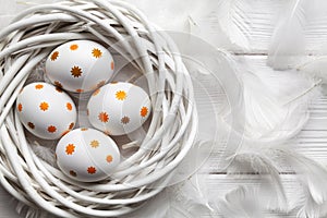 Eastr eggs in the nest and white feathers on table