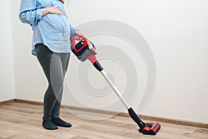 Easy cleaning with a wireless vacuum cleaner. Pregnant woman cleaning floor with handheld vacuum cleaner