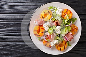 Easy dietary salad with mozzarella, prosciutto, grilled apricots, red onion and lettuce close-up on a plate. horizontal top view